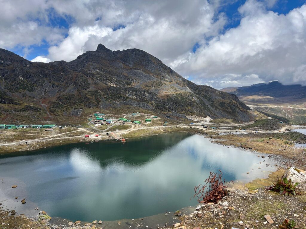 Mirror-still PT Tso near Tawang, snow peaks reflected in clear blue water under a bright sky.
