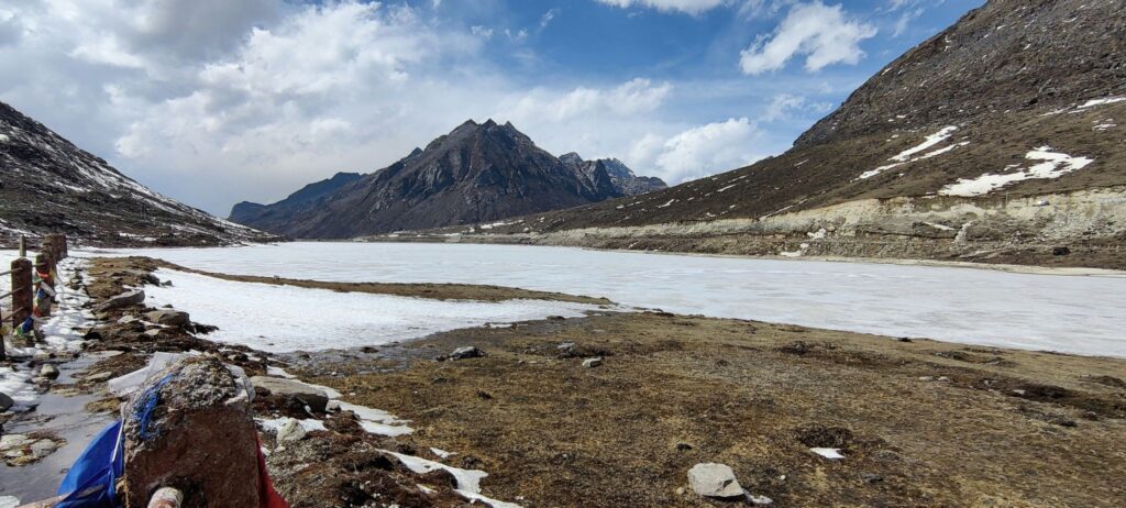 Winding mountain road near Sela Pass with snow on the shoulders and blue sky.
