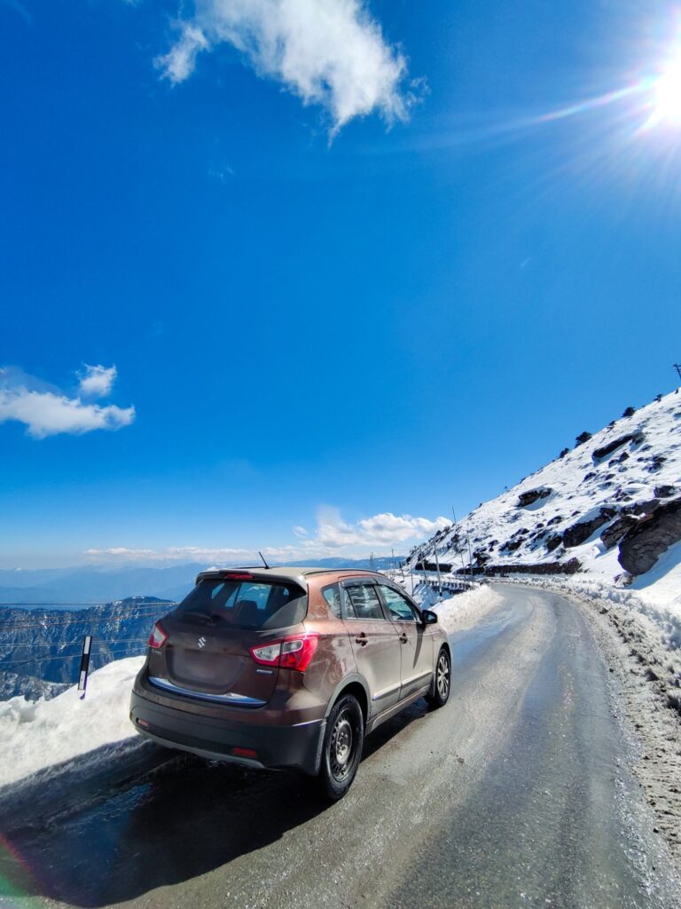 Mountain road near Sela Pass with an SUV stopped on the icy shoulder and snow banks along the curve