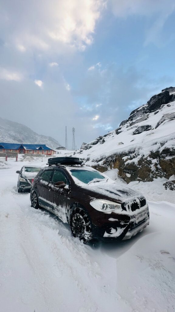 Convoy of SUVs rolling past a snow-lined mountain pass at sunrise.