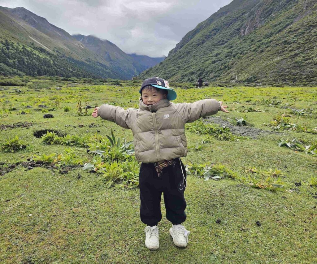 Local kid smiling in a grassy Himalayan valley near Tawang, Arunachal Pradesh, under cloudy skies.